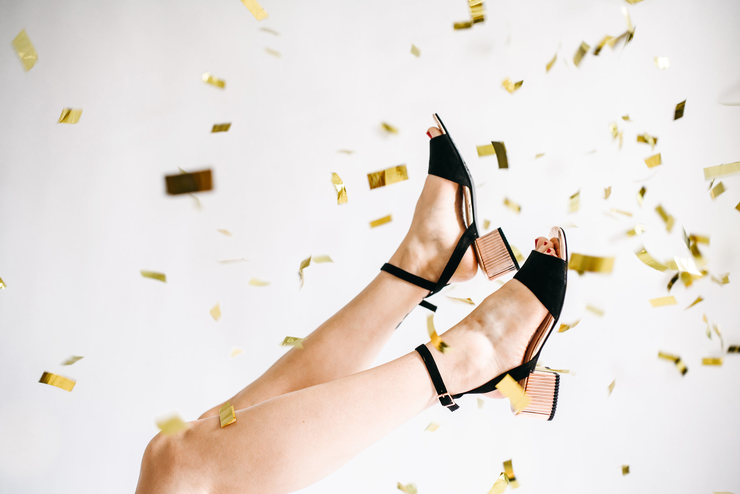 Black heels in the air with gold confetti